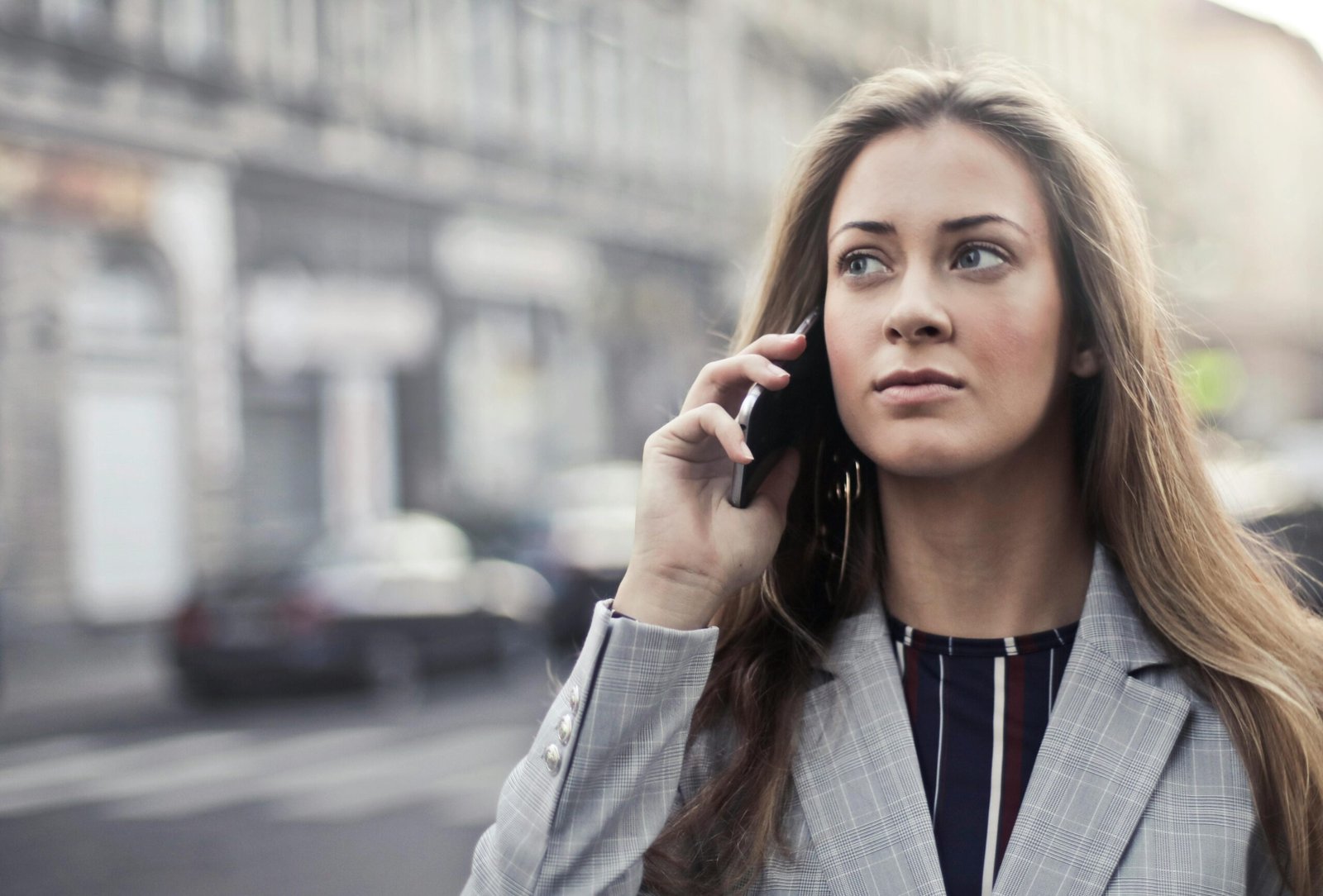 Fashionable young woman talking on smartphone in urban Budapest setting.